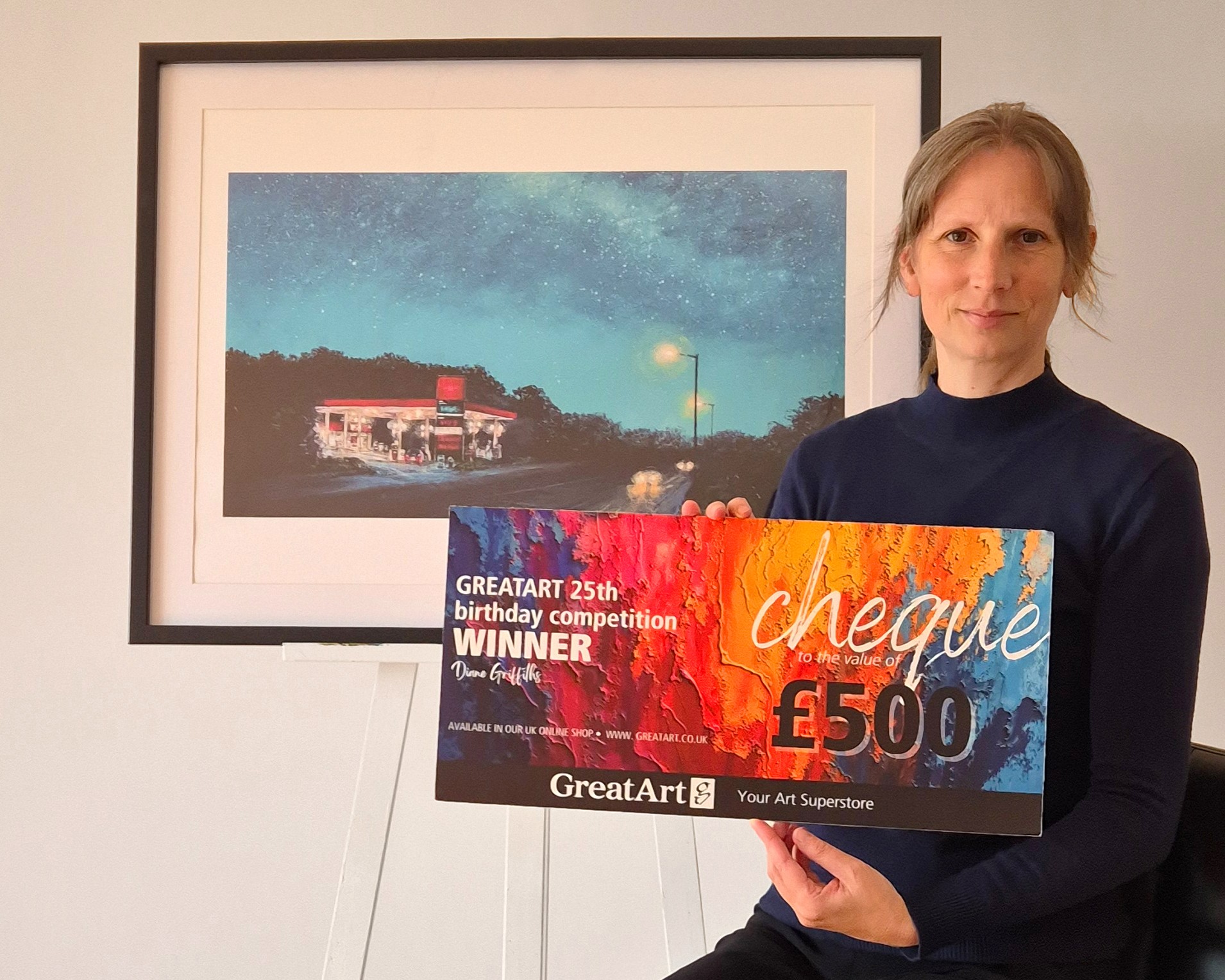 ► Diane holding the winning cheque in front of the winning entry - 'Driving Home'